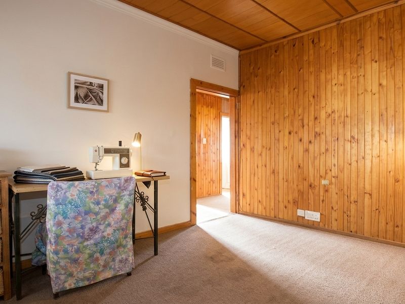 A bedroom featuring timber wall paneling and a timber ceiling, with carpet flooring and a doorway leading to an adjacent room.