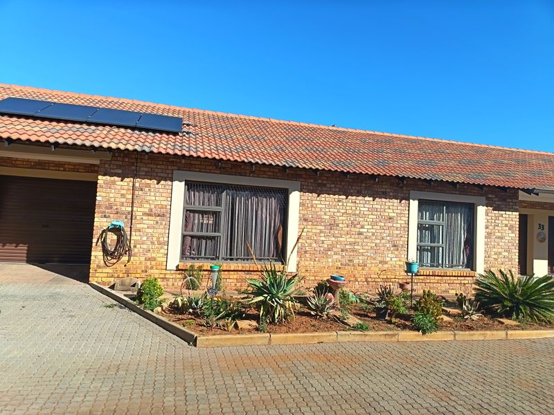 Front elevation of a face brick retirement unit featuring a tiled roof, solar panels, paved driveway, and a single garage.