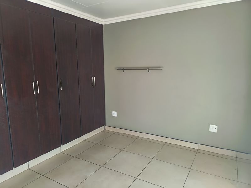 A clean, empty bedroom featuring dark wood built-in cupboards, neutral grey walls, and tiled flooring, providing a versatile space for residents.