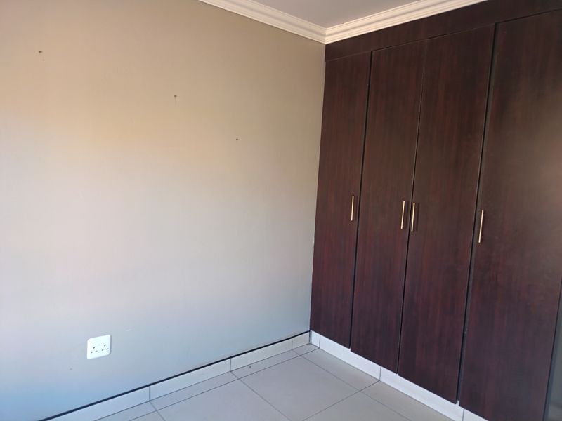 A clean, empty bedroom featuring dark wood built-in cupboards, neutral wall tones, and tiled flooring, providing a versatile space for personalization.