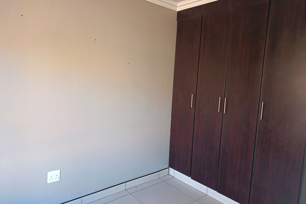A clean, empty bedroom featuring dark wood built-in cupboards, neutral wall tones, and tiled flooring, providing a versatile space for personalization.
