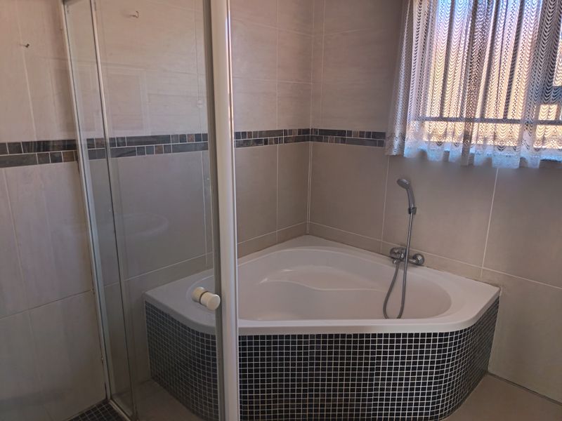 A functional bathroom featuring a corner bathtub with a handheld shower attachment, a separate shower enclosure, and neutral wall tiling with mosaic accents.