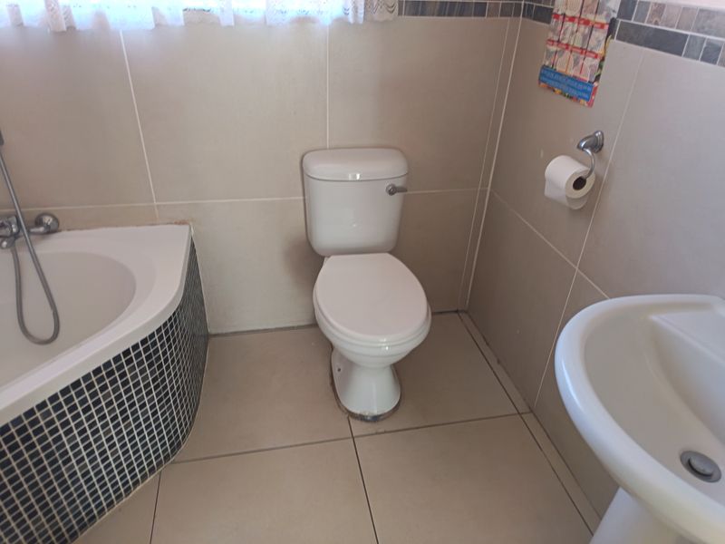 A functional bathroom featuring a pedestal basin, a bathtub with mosaic tile detailing, and neutral wall and floor tiles.