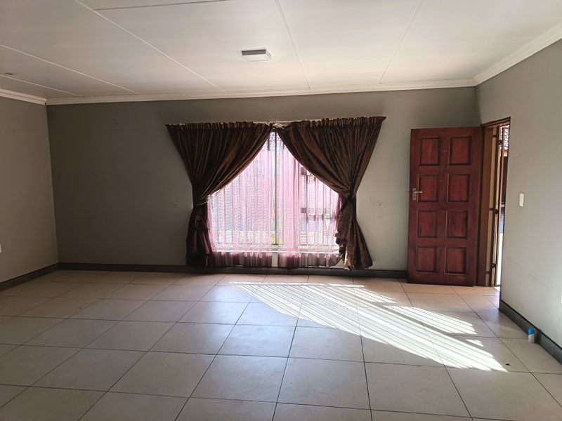 A spacious, empty living area featuring neutral wall tones, tiled flooring, and a classic timber door, offering a blank canvas for personalization.