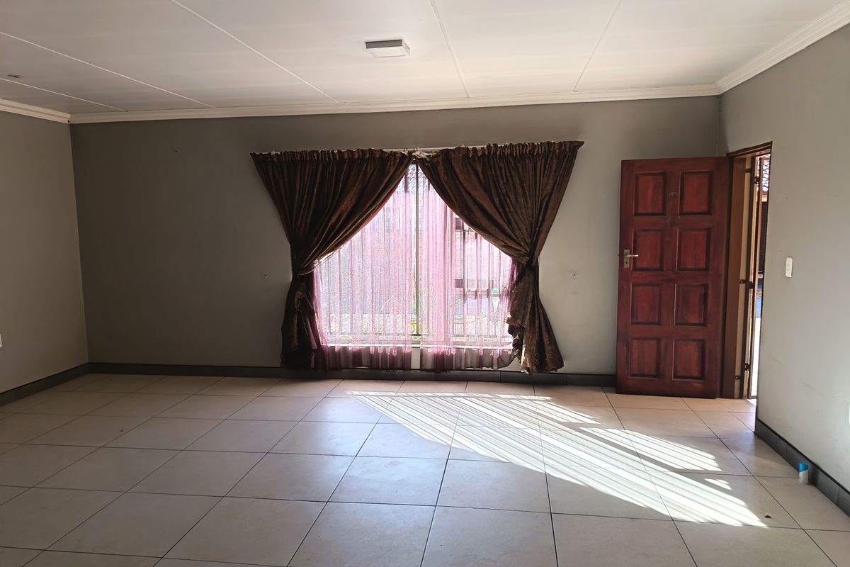A spacious, empty living area featuring neutral wall tones, tiled flooring, and a classic timber door, offering a blank canvas for personalization.