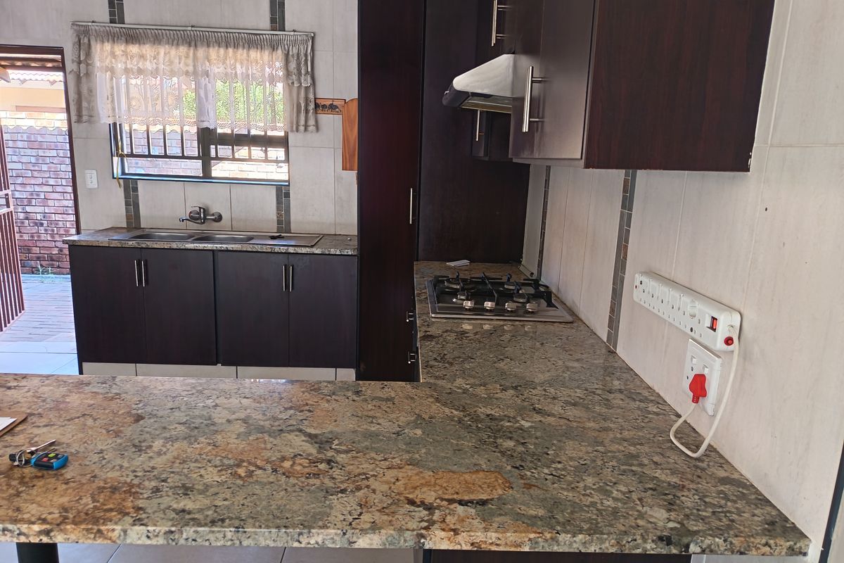 A functional kitchen featuring dark wood cabinetry, granite countertops, a gas hob with extractor fan, and a double stainless steel sink with tiled splashbacks.