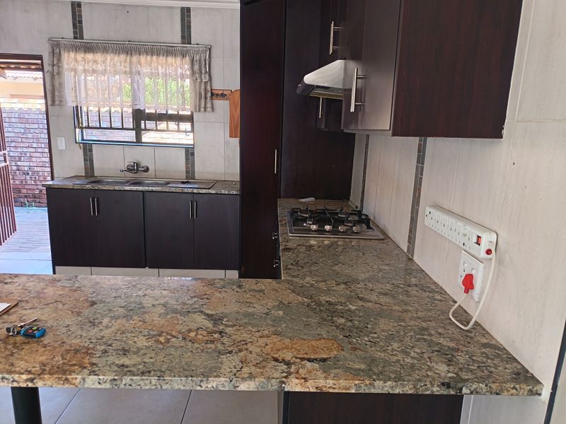 A functional kitchen featuring dark wood cabinetry, granite countertops, a gas hob with extractor fan, and a double stainless steel sink with tiled splashbacks.