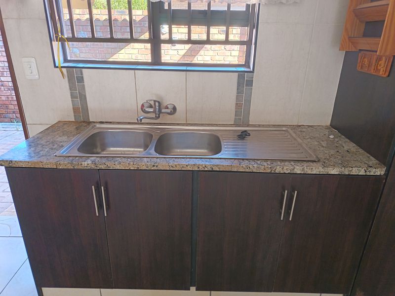 A functional kitchen area featuring a double bowl stainless steel sink, granite countertops, and dark wood cabinetry with a tiled backsplash.