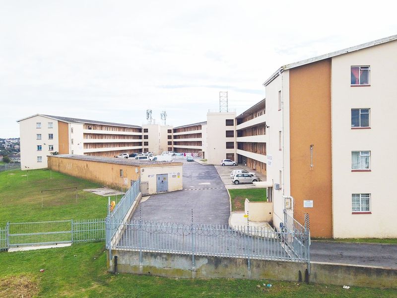 Aerial view of a multi-story apartment complex featuring paved driveway access, perimeter security fencing, and exterior building facades.