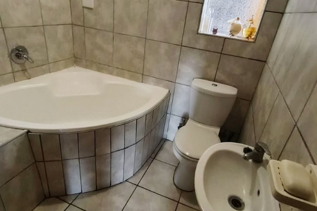 A compact bathroom featuring a corner bathtub, pedestal basin, and toilet, finished with neutral ceramic tiling throughout.