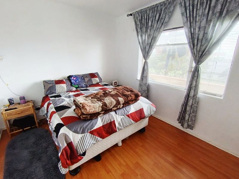 A bedroom featuring laminate flooring and window blinds, offering a functional space with neutral wall finishes.