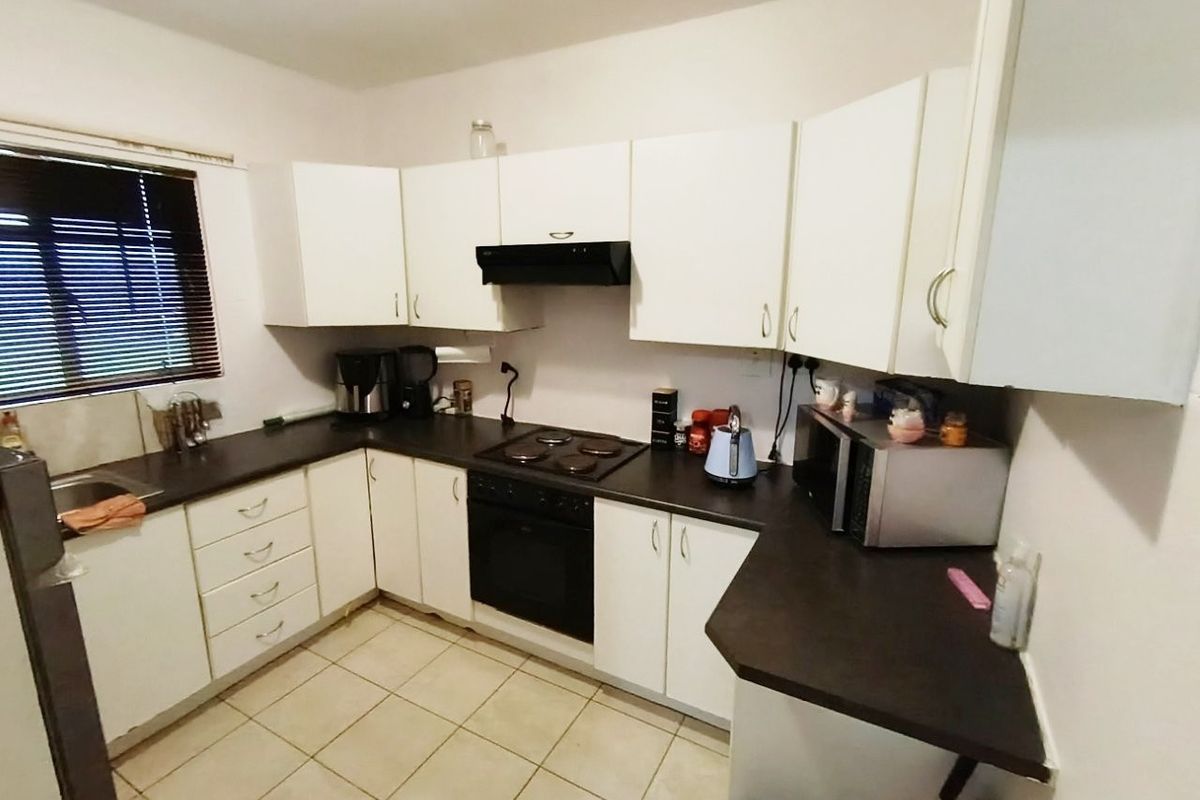 A functional kitchen featuring white cabinetry, dark laminate countertops, an integrated electric hob and oven, and tiled flooring.