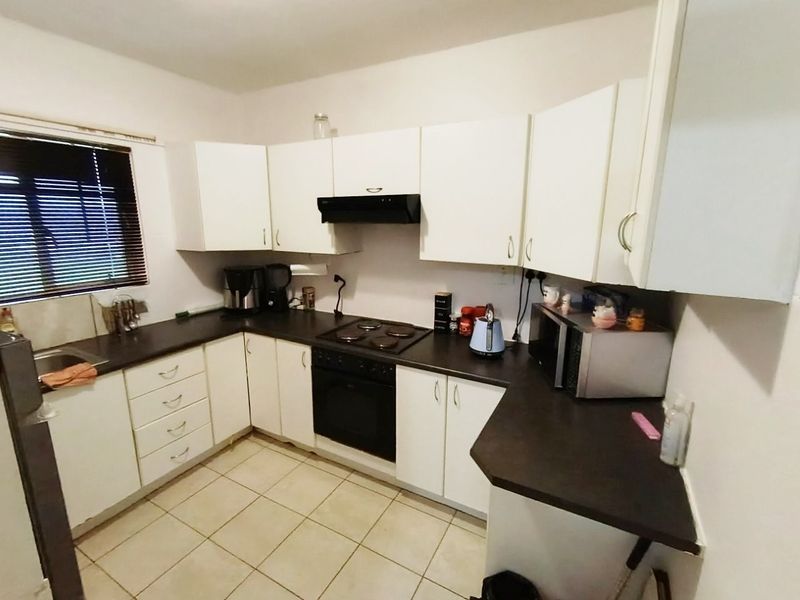 A functional kitchen featuring white cabinetry, dark laminate countertops, an integrated electric hob and oven, and tiled flooring.