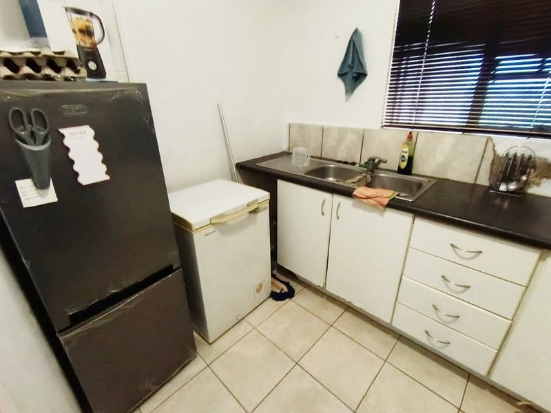 A functional kitchen area featuring built-in cabinetry, a double sink, tiled backsplash, and tiled flooring, requiring some cosmetic updates to the wall and cabinetry finishes.