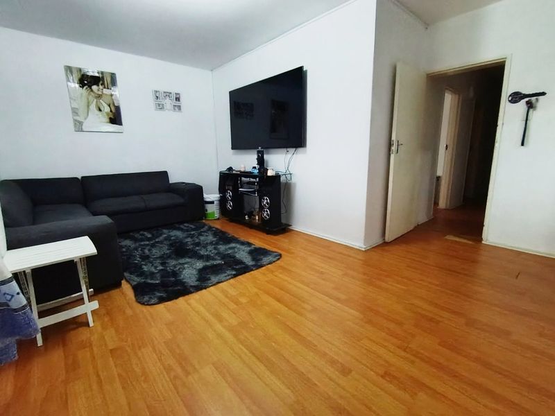 A living room featuring laminate flooring and access to an adjoining hallway.