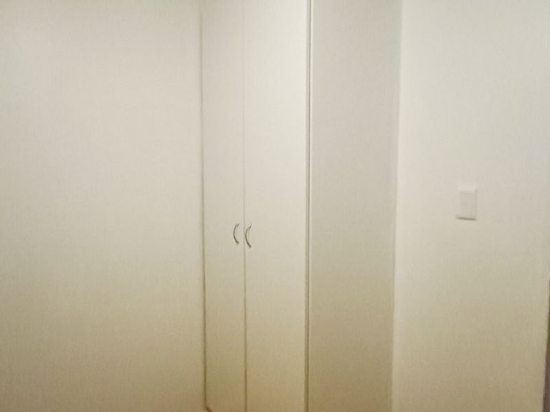 A simple bedroom space featuring a built-in white wardrobe and laminate flooring, offering a clean and functional storage solution.