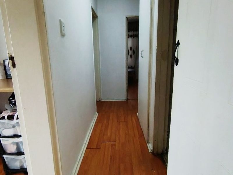 A narrow hallway featuring laminate flooring and access to multiple rooms, showing signs of wear on the floor and door frames.