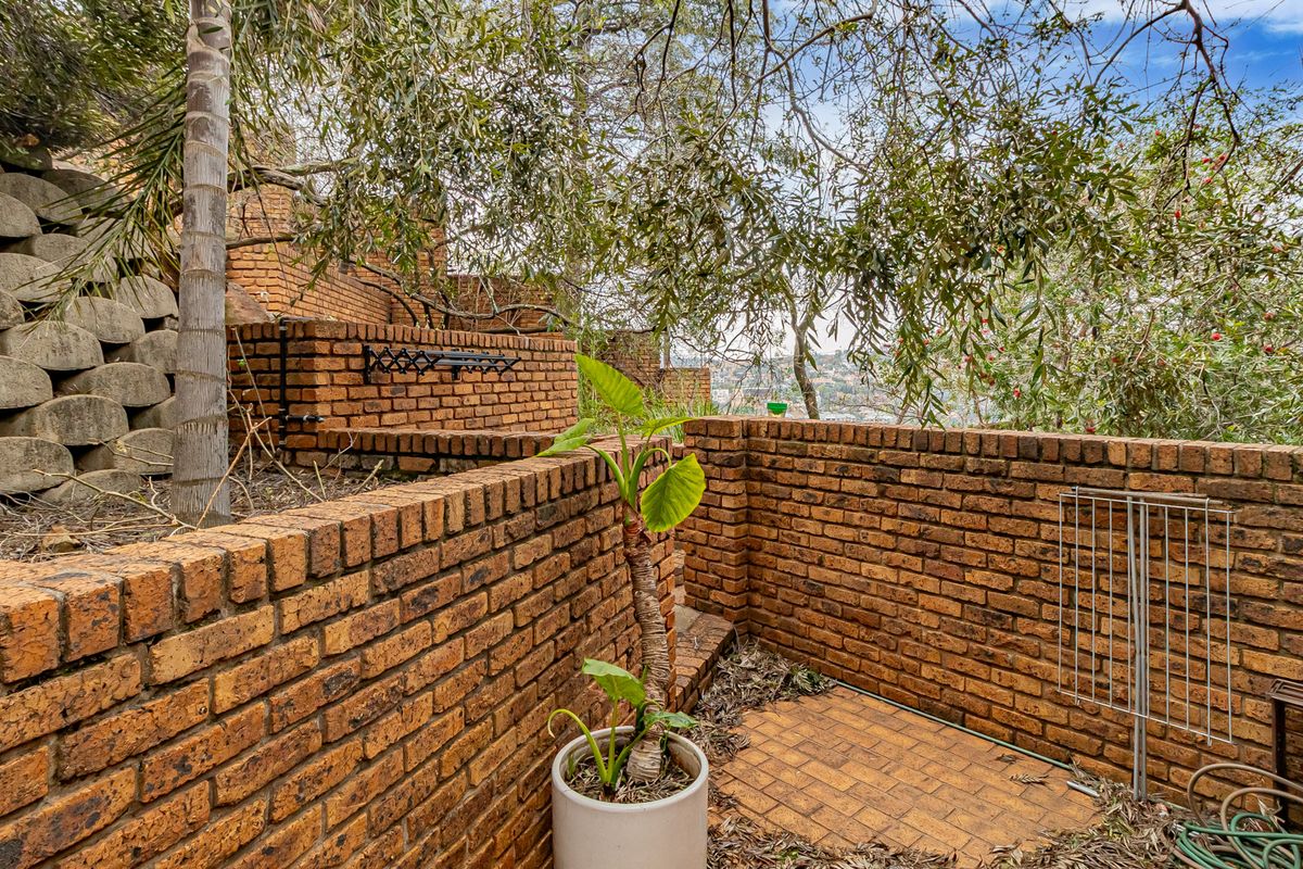 A tiered rear garden area featuring rustic brick retaining walls and paved sections, set against a backdrop of mature trees and hillside views.