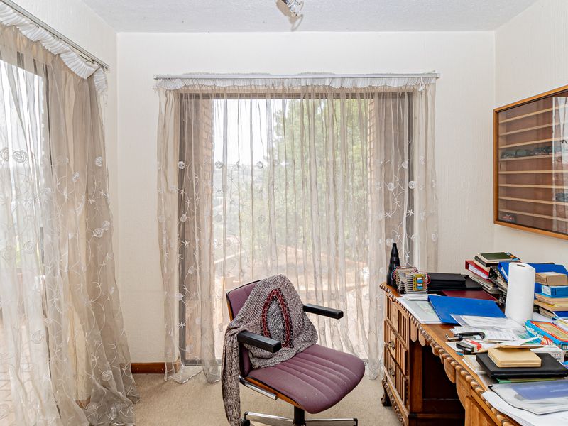 A functional home office space featuring carpeted flooring, a built-in display cabinet, and large sliding glass doors providing natural light and outdoor access.