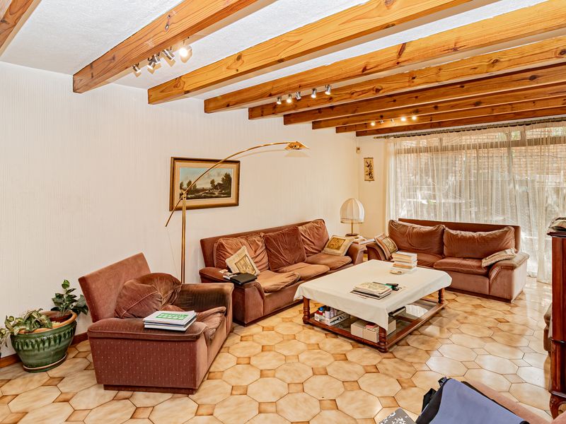 A living room featuring exposed timber ceiling beams, ceramic tile flooring, and a large sliding glass door providing natural light.