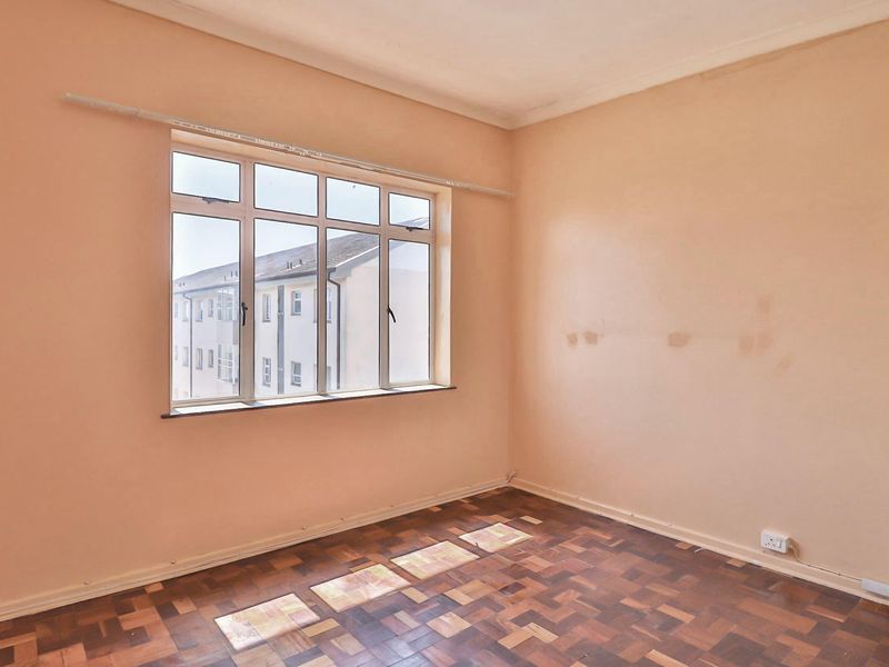 An empty bedroom featuring parquet flooring and a large multi-pane window, requiring cosmetic updates to the wall surfaces.