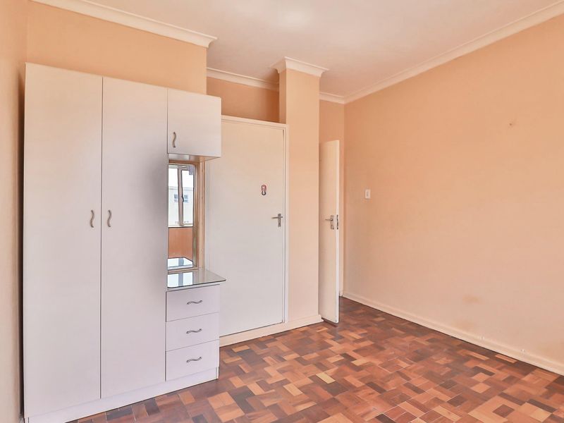 A vacant bedroom featuring parquet flooring, built-in wardrobe cabinetry, and neutral wall finishes, offering a clean canvas for personalization.