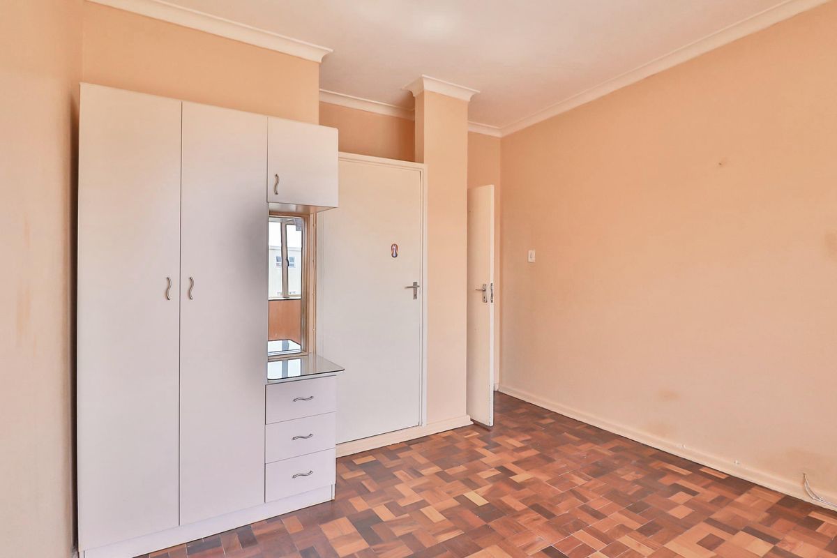 A vacant bedroom featuring parquet flooring, built-in wardrobe cabinetry, and neutral wall finishes, offering a clean canvas for personalization.