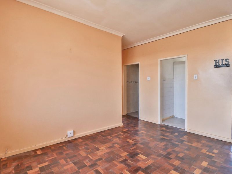 An empty living area featuring traditional parquet flooring and neutral wall tones, providing a blank canvas for renovation or interior design updates.