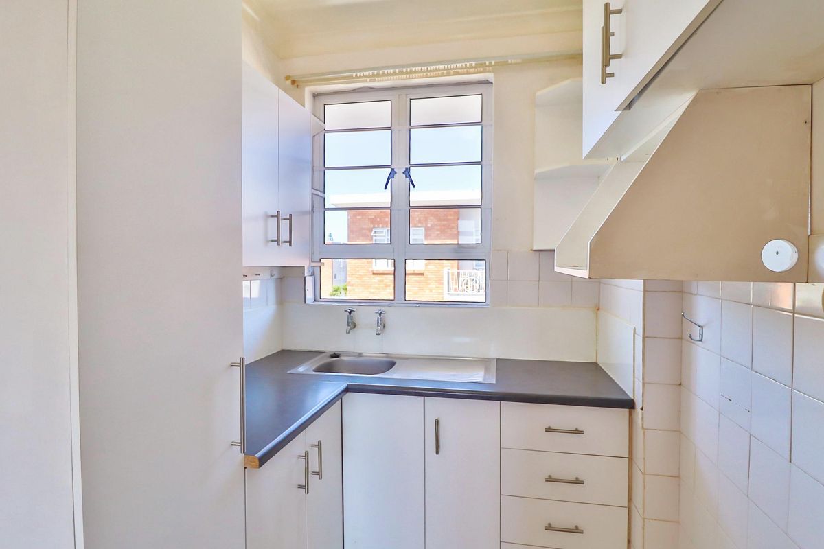 A compact, functional kitchen featuring white built-in cabinetry, a dark laminate countertop, a stainless steel sink, and a tiled backsplash.