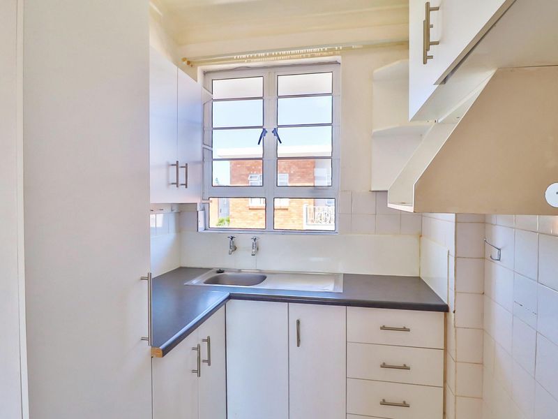 A compact, functional kitchen featuring white built-in cabinetry, a dark laminate countertop, a stainless steel sink, and a tiled backsplash.