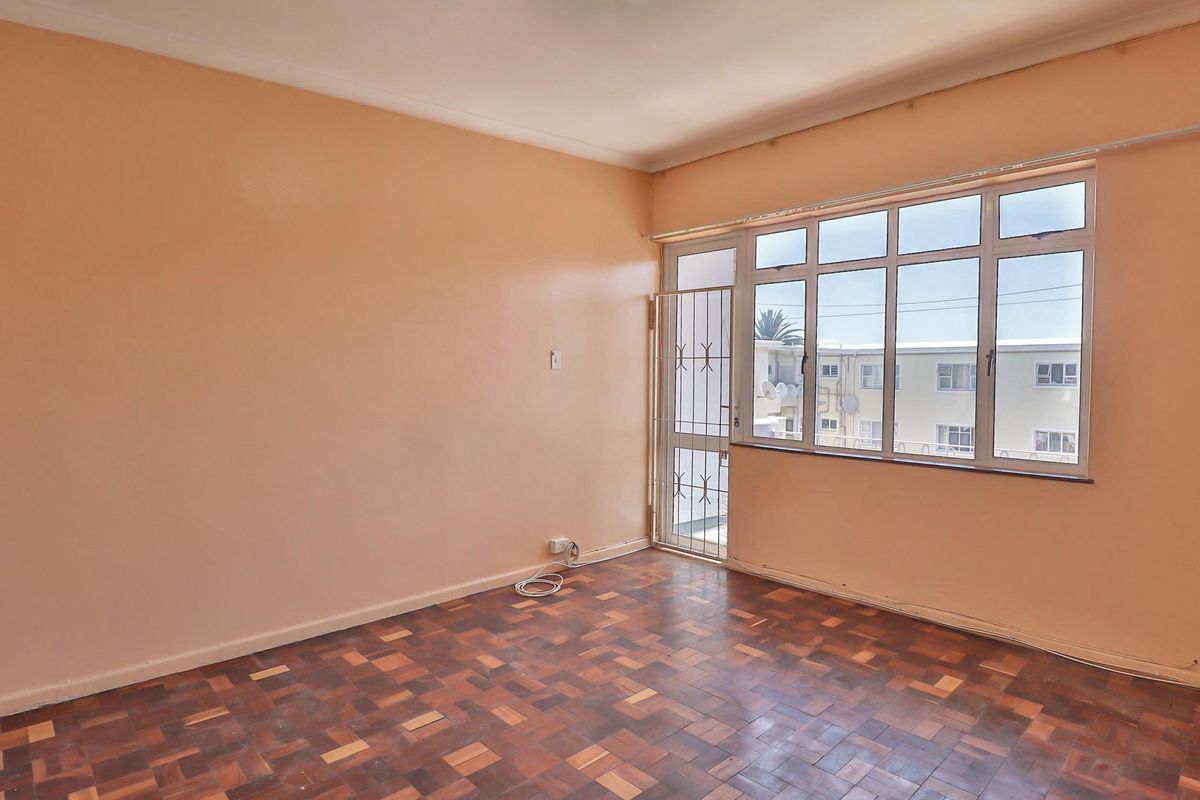 An empty living room featuring classic parquet flooring, large windows for natural light, and a secure metal gate leading to the exterior.