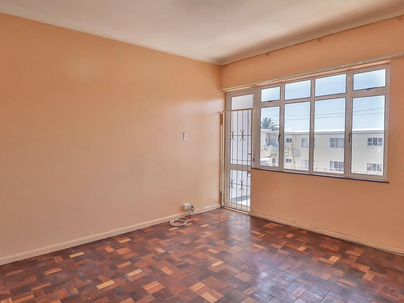 An empty living room featuring classic parquet flooring, large windows for natural light, and a secure metal gate leading to the exterior.