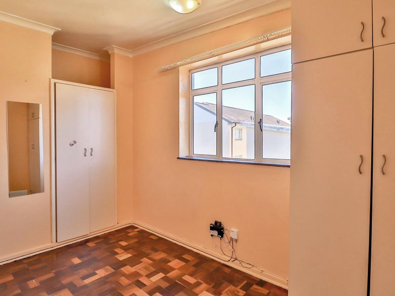 A bright, empty bedroom featuring classic parquet flooring, built-in storage cupboards, and a window providing natural light.