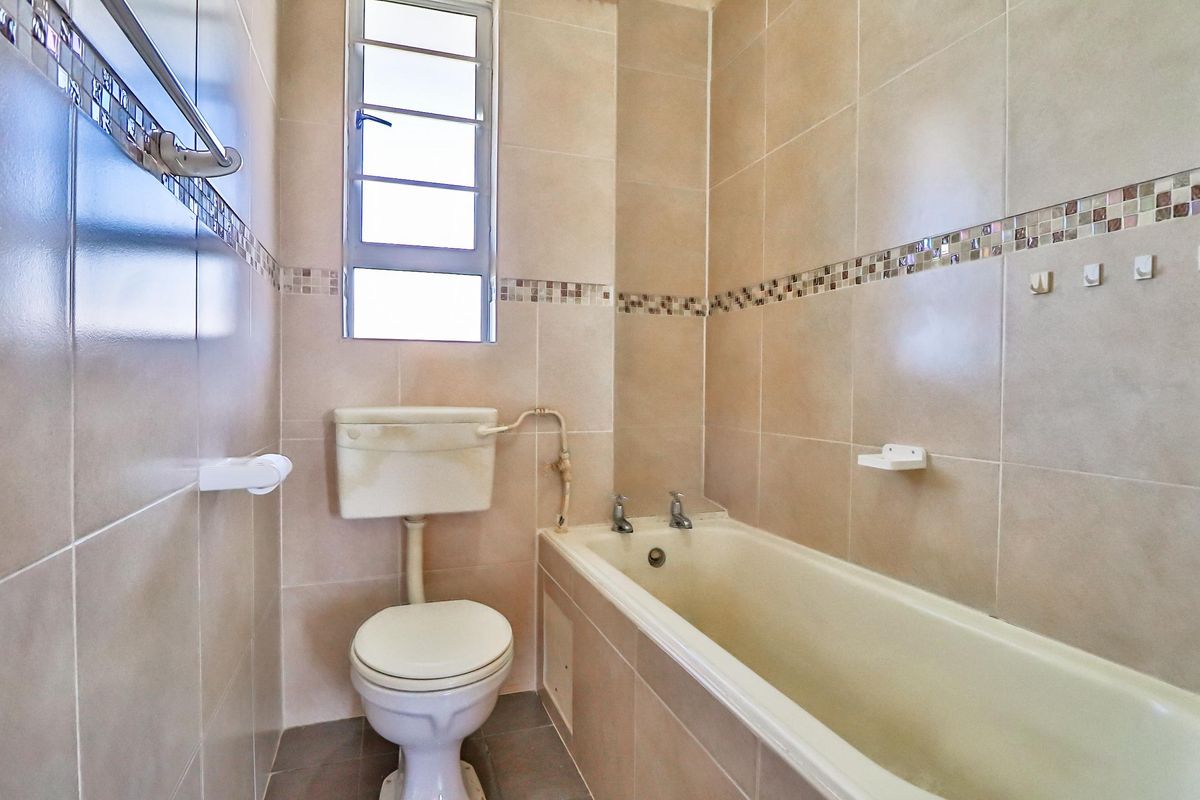 A compact bathroom featuring full-height wall tiling, a standard bathtub, and a toilet, requiring cosmetic updates to modernize the dated fixtures.