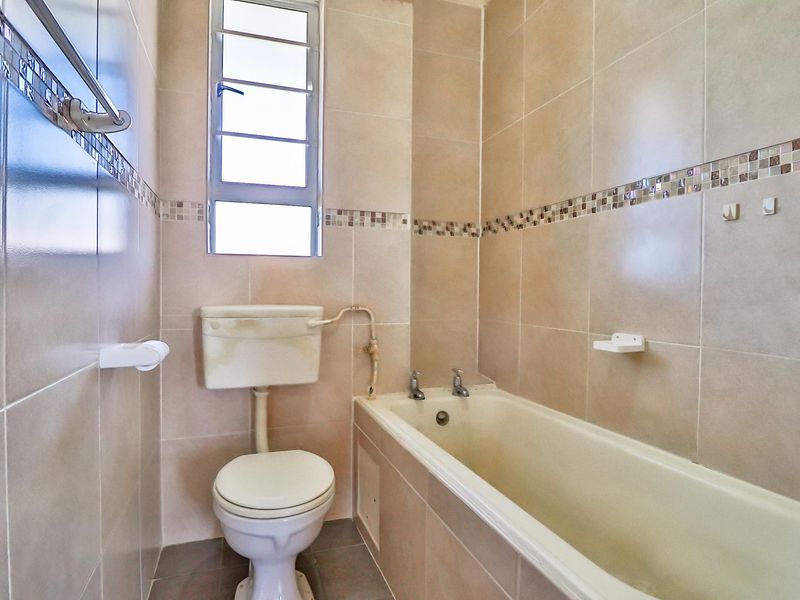 A compact bathroom featuring full-height wall tiling, a standard bathtub, and a toilet, requiring cosmetic updates to modernize the dated fixtures.