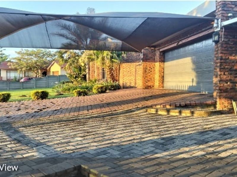 Front exterior view featuring a brick driveway with shade sail covering, a garage door, and surrounding brick facade.