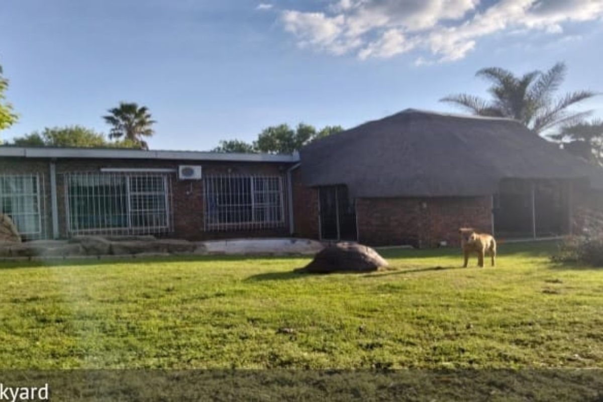 Rear view of the property featuring a brick facade, a traditional thatch roof section, and a spacious garden area.