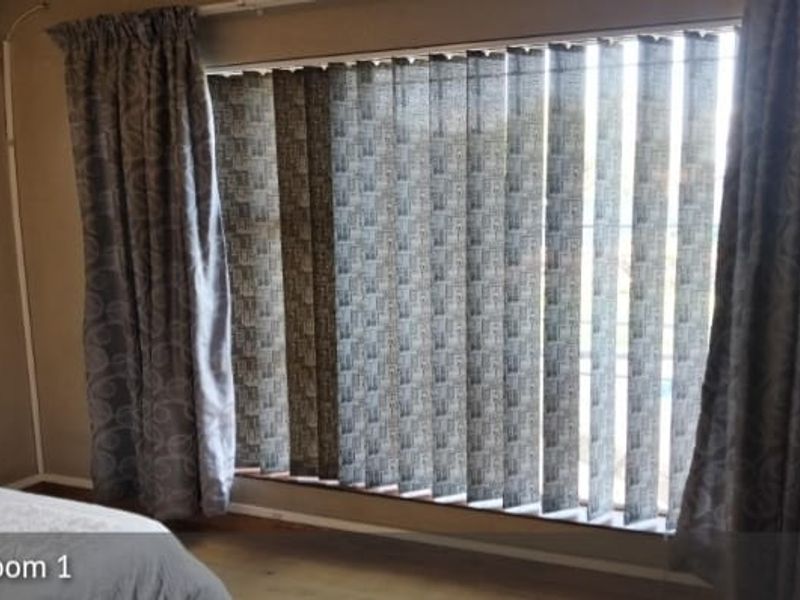 A bedroom featuring a large window with vertical blinds and curtain tracks, providing natural light and privacy.