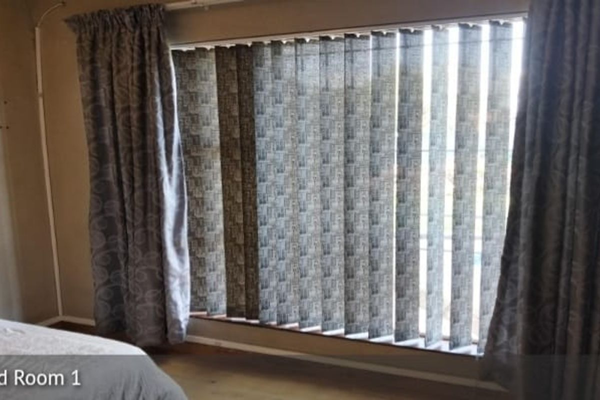 A bedroom featuring a large window with vertical blinds and curtain tracks, providing natural light and privacy.