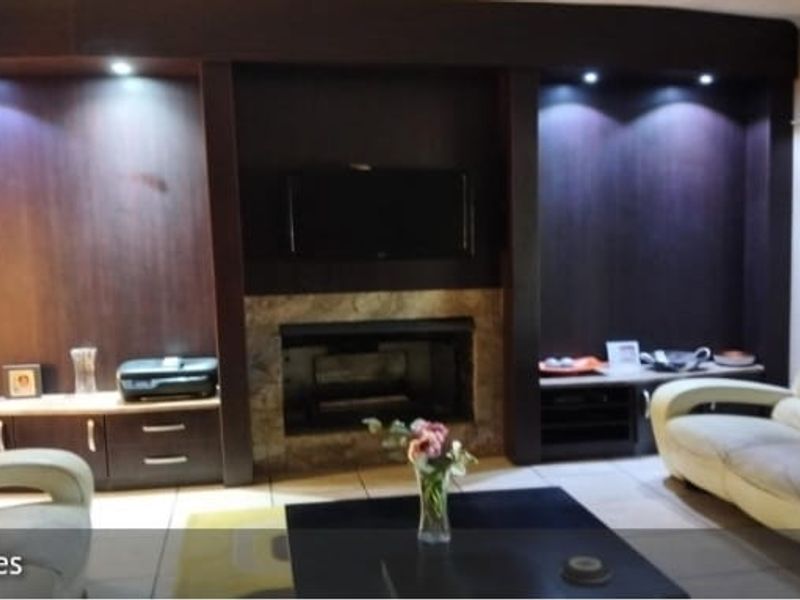 Spacious living room featuring a prominent built-in dark wood entertainment unit with integrated fireplace, recessed lighting, and neutral tiled flooring.