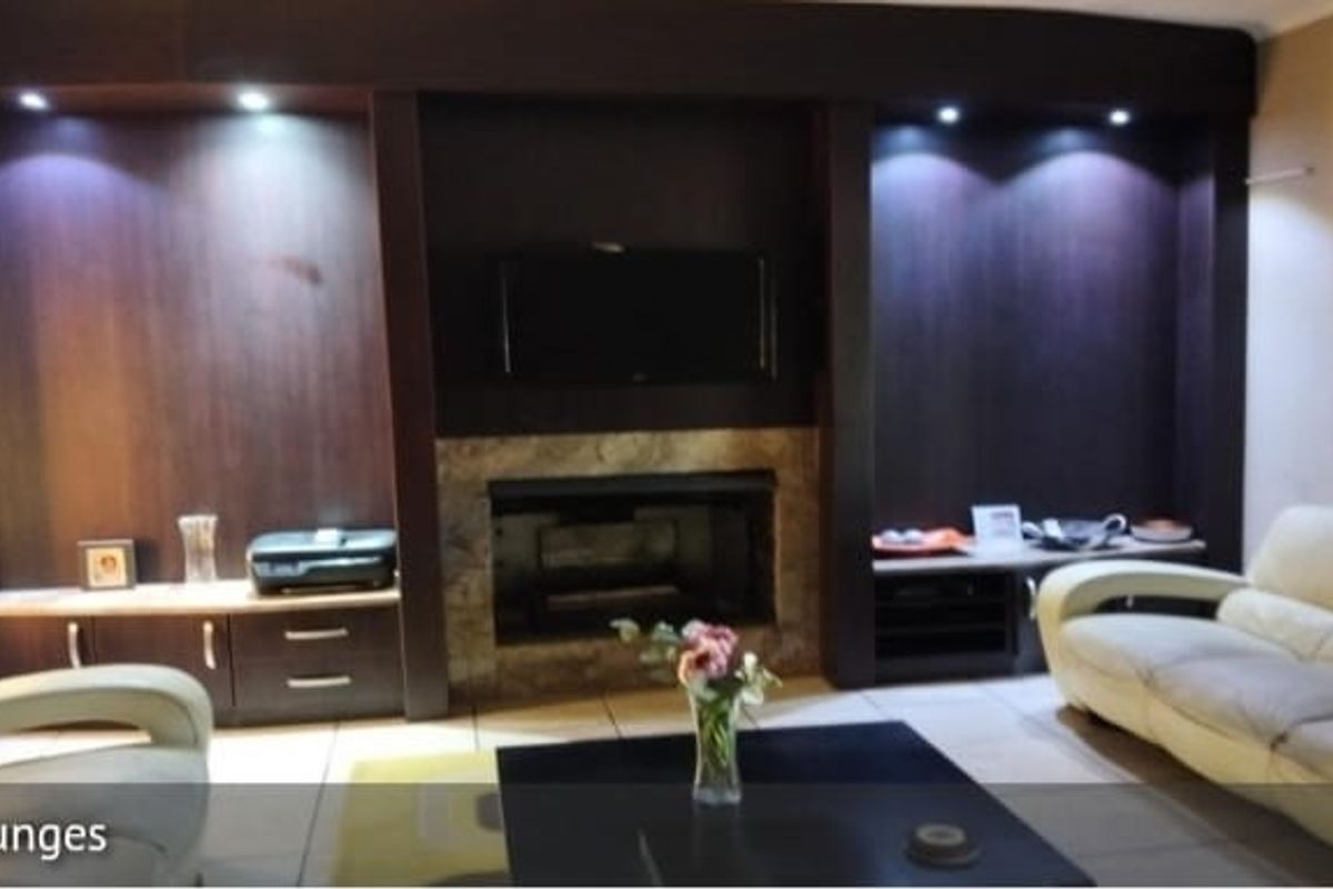Spacious living room featuring a prominent built-in dark wood entertainment unit with integrated fireplace, recessed lighting, and neutral tiled flooring.