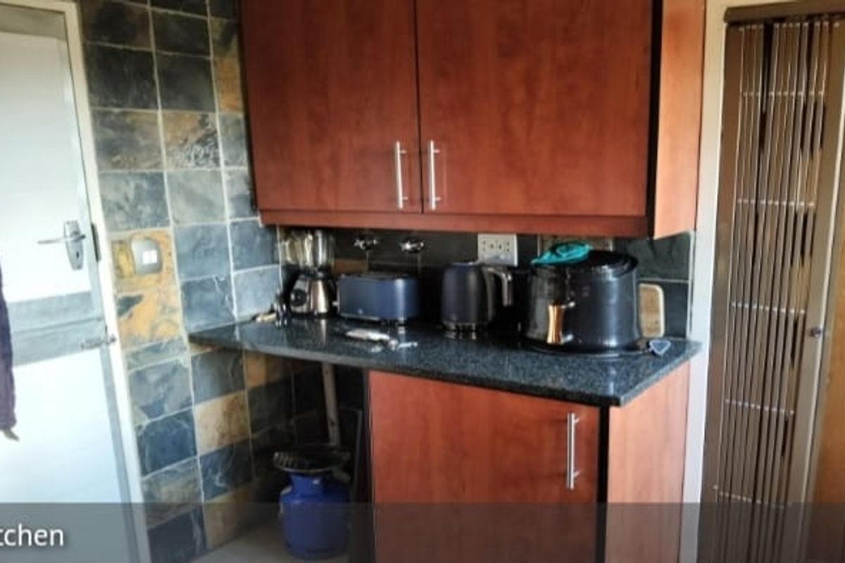 A compact kitchen area featuring dark wood cabinetry, granite countertops, and slate tile backsplash, offering a functional prep space with potential for modernization.