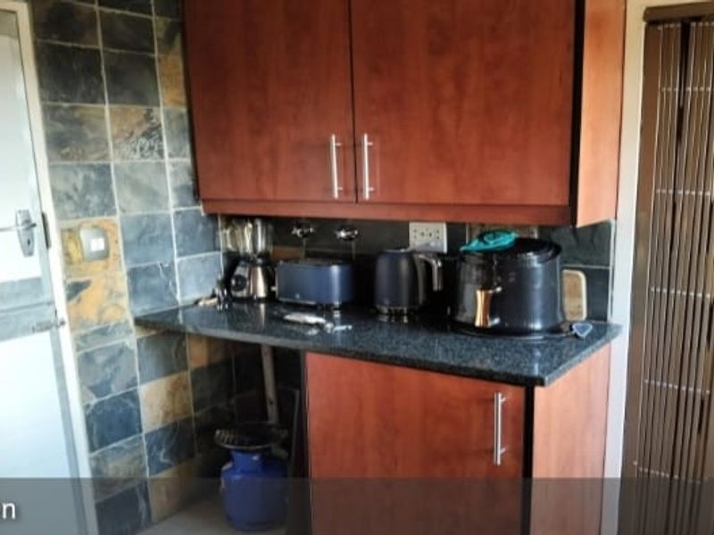 A compact kitchen area featuring dark wood cabinetry, granite countertops, and slate tile backsplash, offering a functional prep space with potential for modernization.