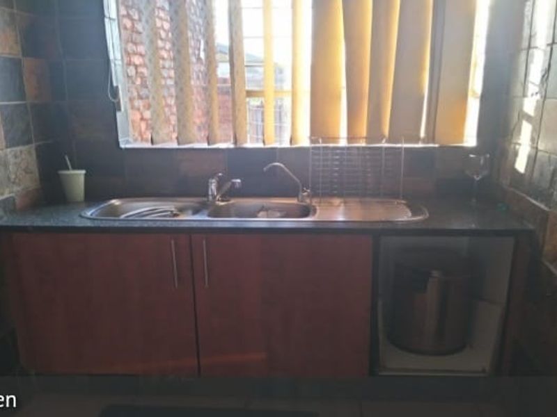 A compact kitchen area featuring a double bowl stainless steel sink, laminate cabinetry, and dark stone tile wall finishes.