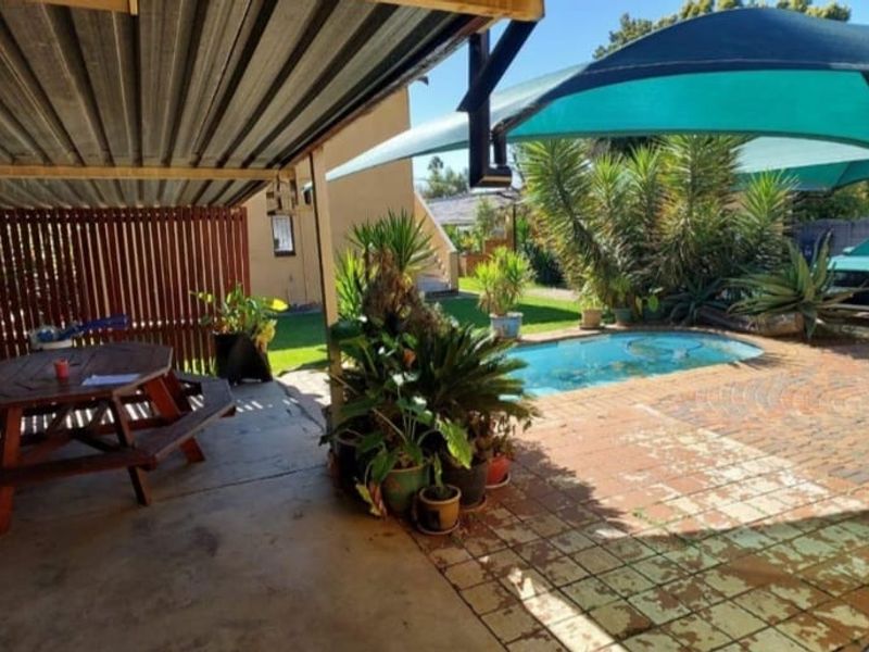 Covered patio area featuring a timber privacy screen, overlooking a swimming pool with brick paving and a shade sail.