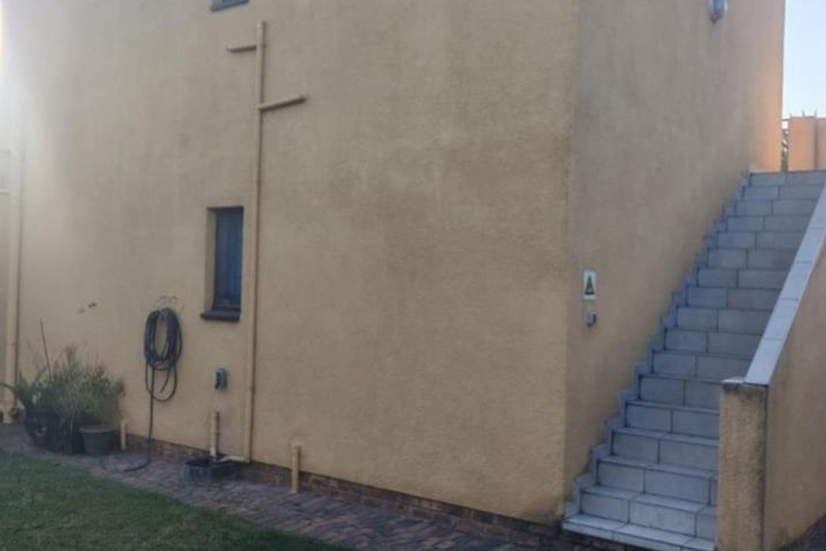 Rear exterior view of the property featuring a paved walkway, external staircase, and plastered wall finish.