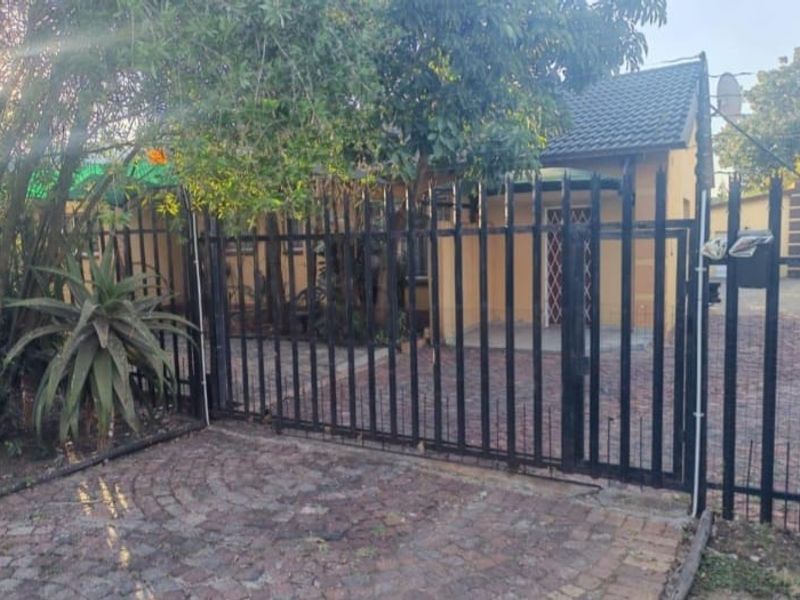 Front view of the property featuring a paved driveway, secure metal perimeter fencing, and a tiled roof entrance.
