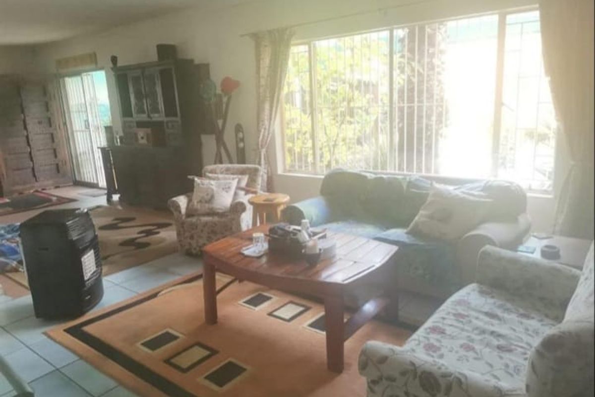A spacious living room featuring tiled flooring, large windows with security bars, and a sliding door providing access to the exterior.