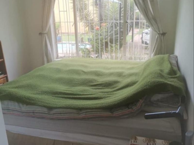 A bedroom featuring tiled flooring and a large window fitted with security bars, offering a view of the outdoor area.