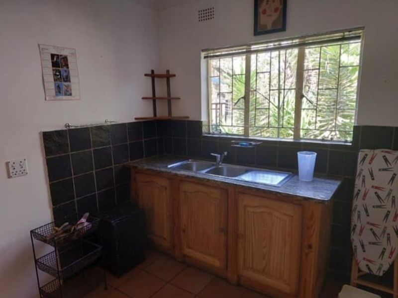 A functional scullery area featuring wooden cabinetry, a double basin sink, and dark tiled splashbacks with a window overlooking the garden.